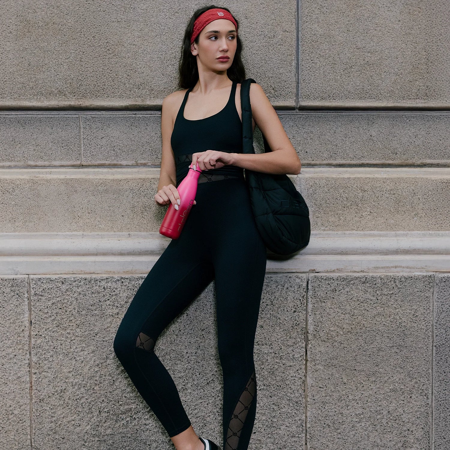Woman in black activewear leggings and top with a red headband holding a pink water bottle