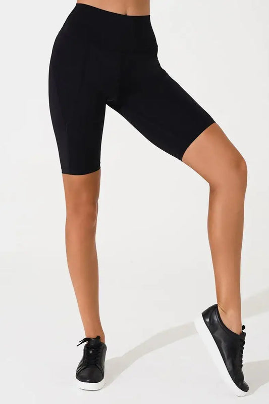 Woman wearing high-waisted black biker shorts and black sneakers on white background
